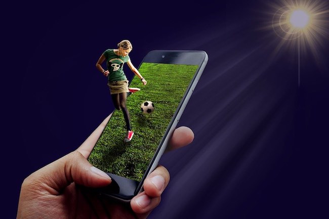 You woman juggling soccer ball while coming out of mobile phone