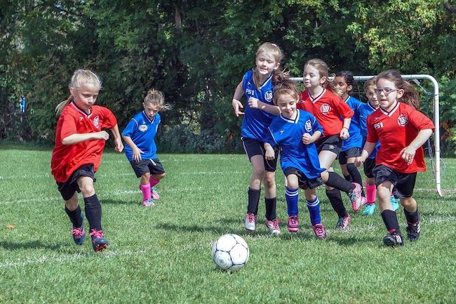 Girls playing a soccer game and all chasing after the ball