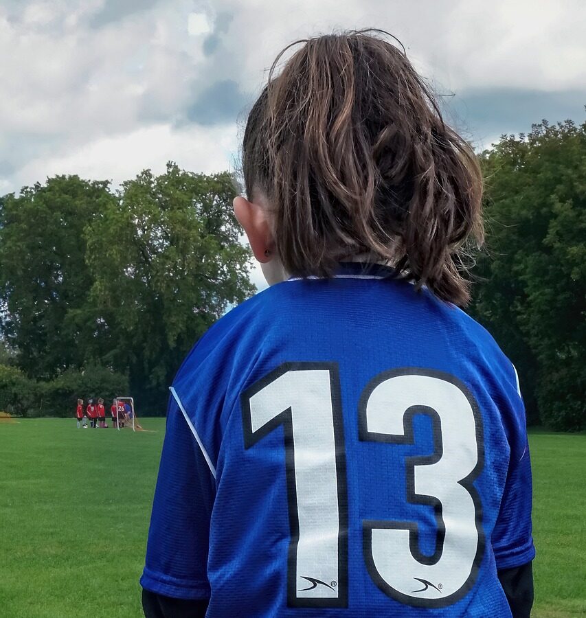 Girl with a soccer jersey sitting on the bench at a soccer field